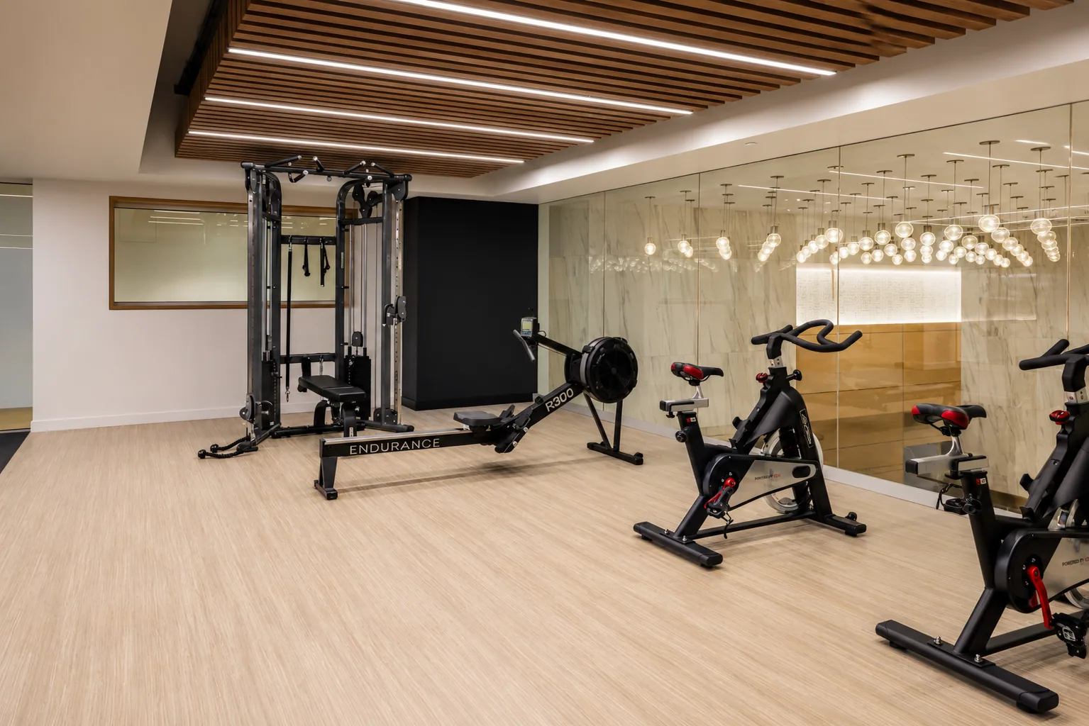 Fitness room on the mezzanine of an Uptown Charlotte office building with a cable machine, rower, bikes and a marble-pattern glass wall, an amenity design by Ossa Studio