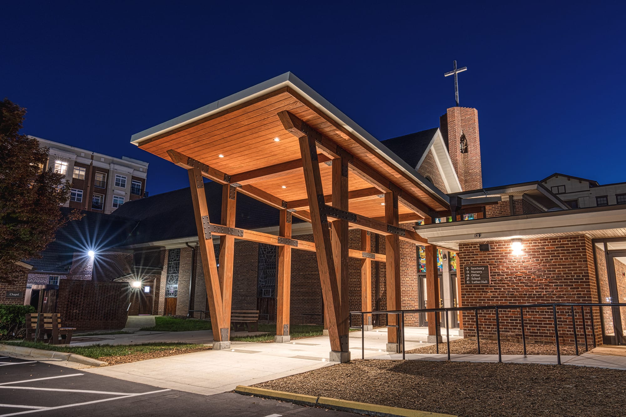 Ascension Church entry canopy in Charlotte, NC at night with recessed lights in the wood roof and the brick tower by Ossa Studio