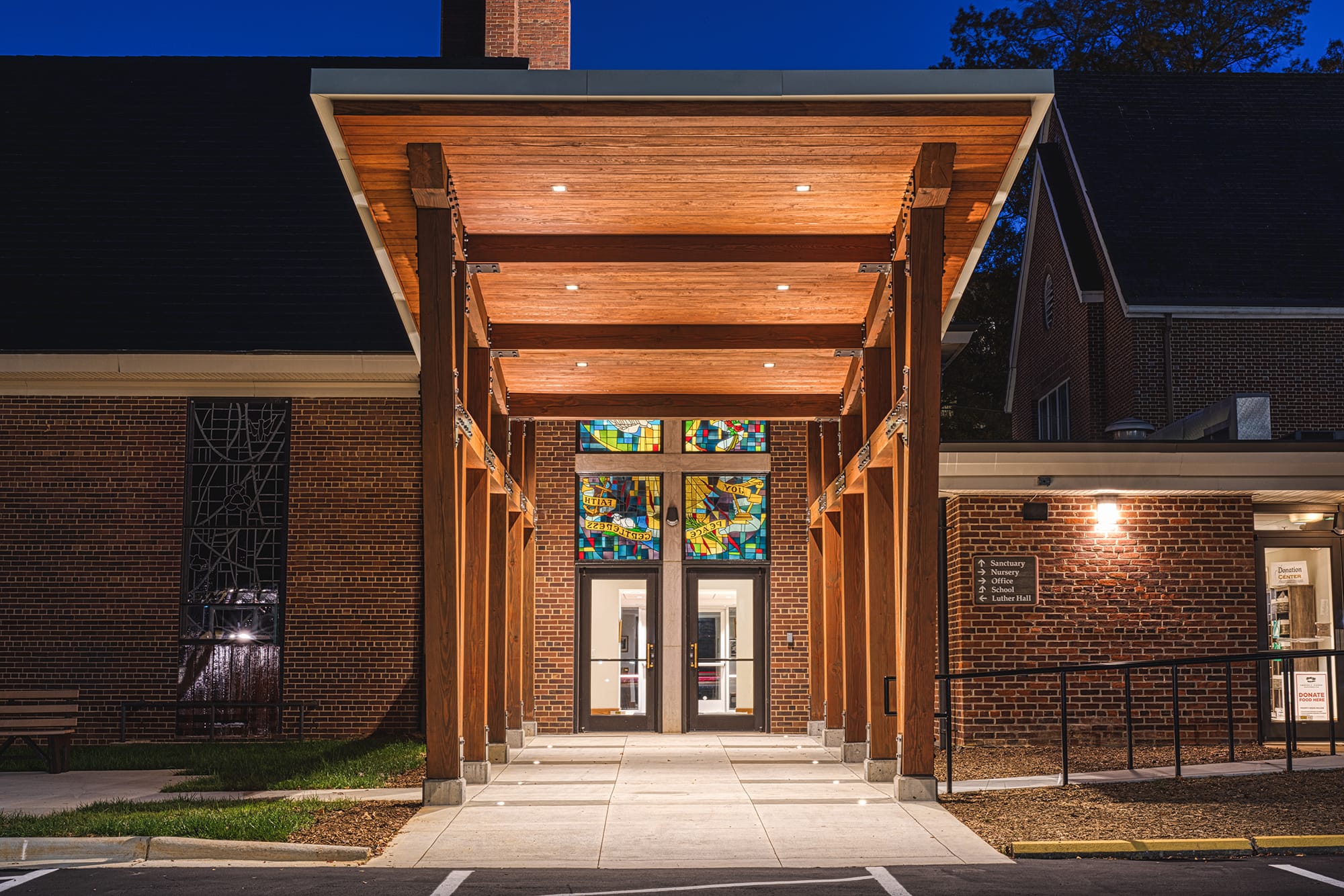 Night view down the lit timber canopy at Ascension Church in Charlotte, NC toward the stained glass entry doors by Ossa Studio