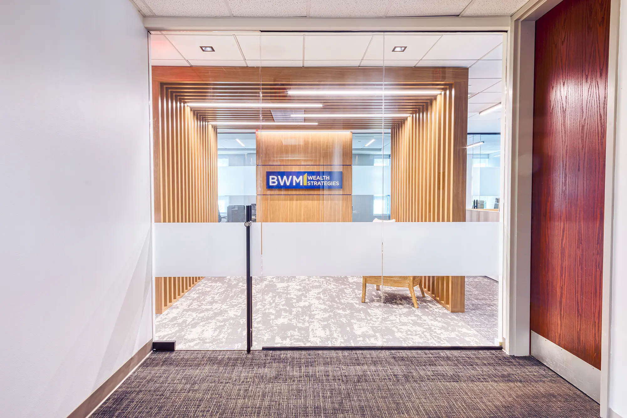 BWM Wealth Strategies office entrance in Charlotte, NC, with glass doors, custom wood slats and branded reception wall by Ossa Studio.