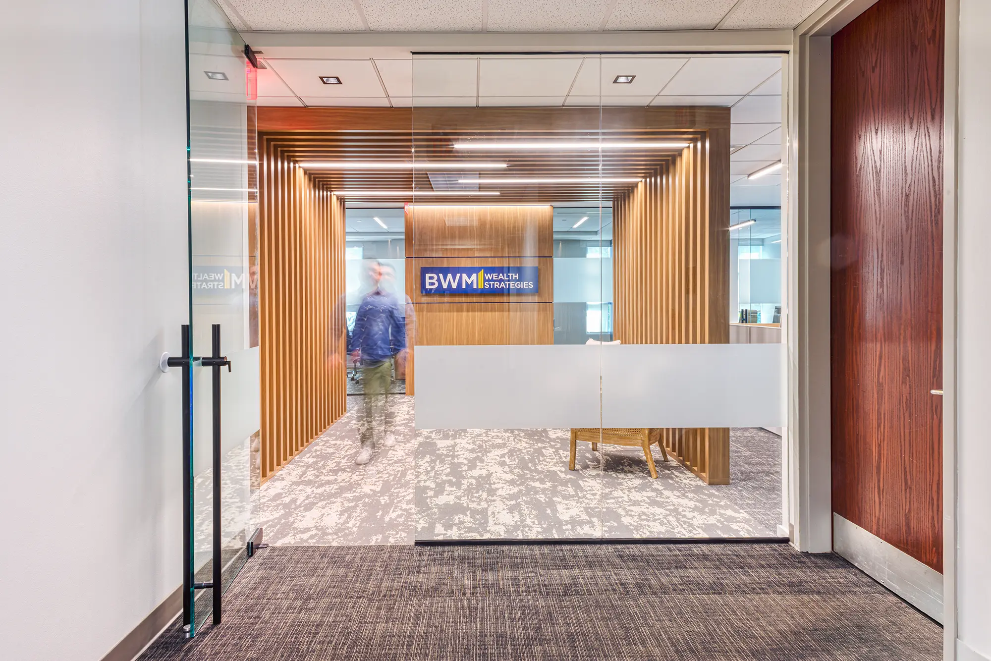Glass entrance to the BWM Wealth Strategies office in Charlotte, NC, highlighting the illuminated wood reception feature by Ossa Studio.