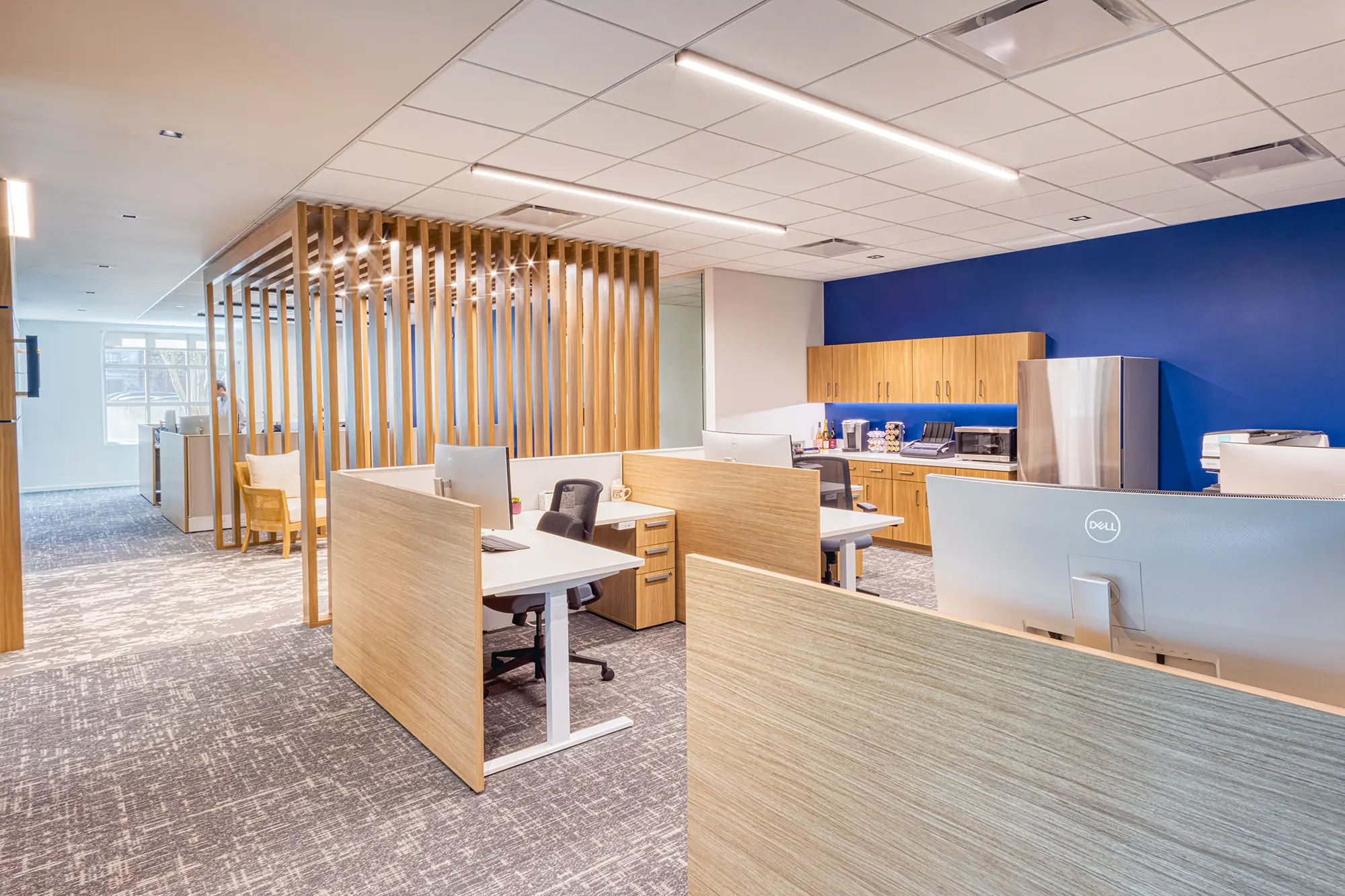 Open office at BWM Wealth Strategies in Charlotte, NC, featuring wood workstations, blue accents and a slatted wood feature designed by Ossa Studio.