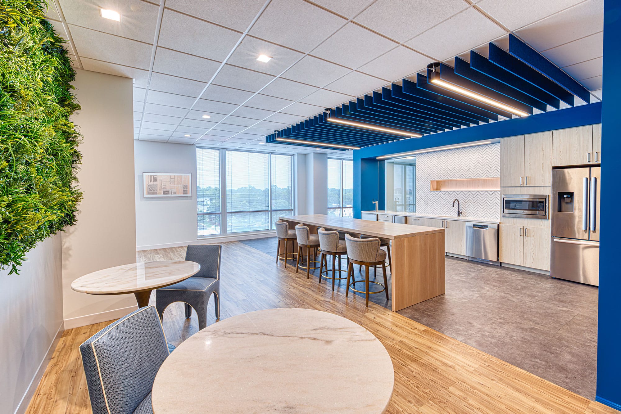 Break area in the Collet office in Charlotte, NC with a green wall, bar-height island, round tables and large windows by Ossa Studio