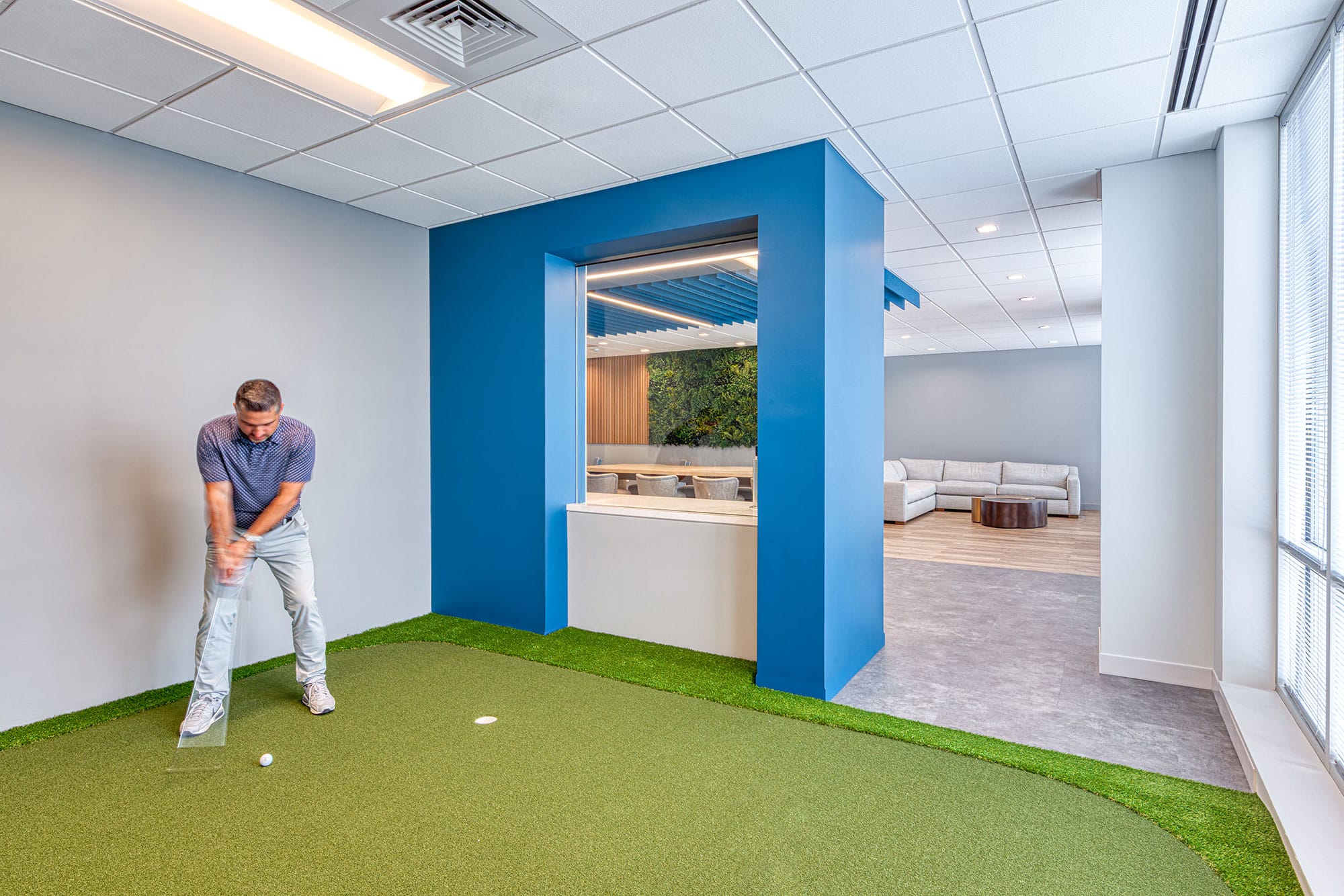 Indoor putting green at the Collet office in Charlotte, NC framed by a blue portal, with the lounge beyond, by Ossa Studio