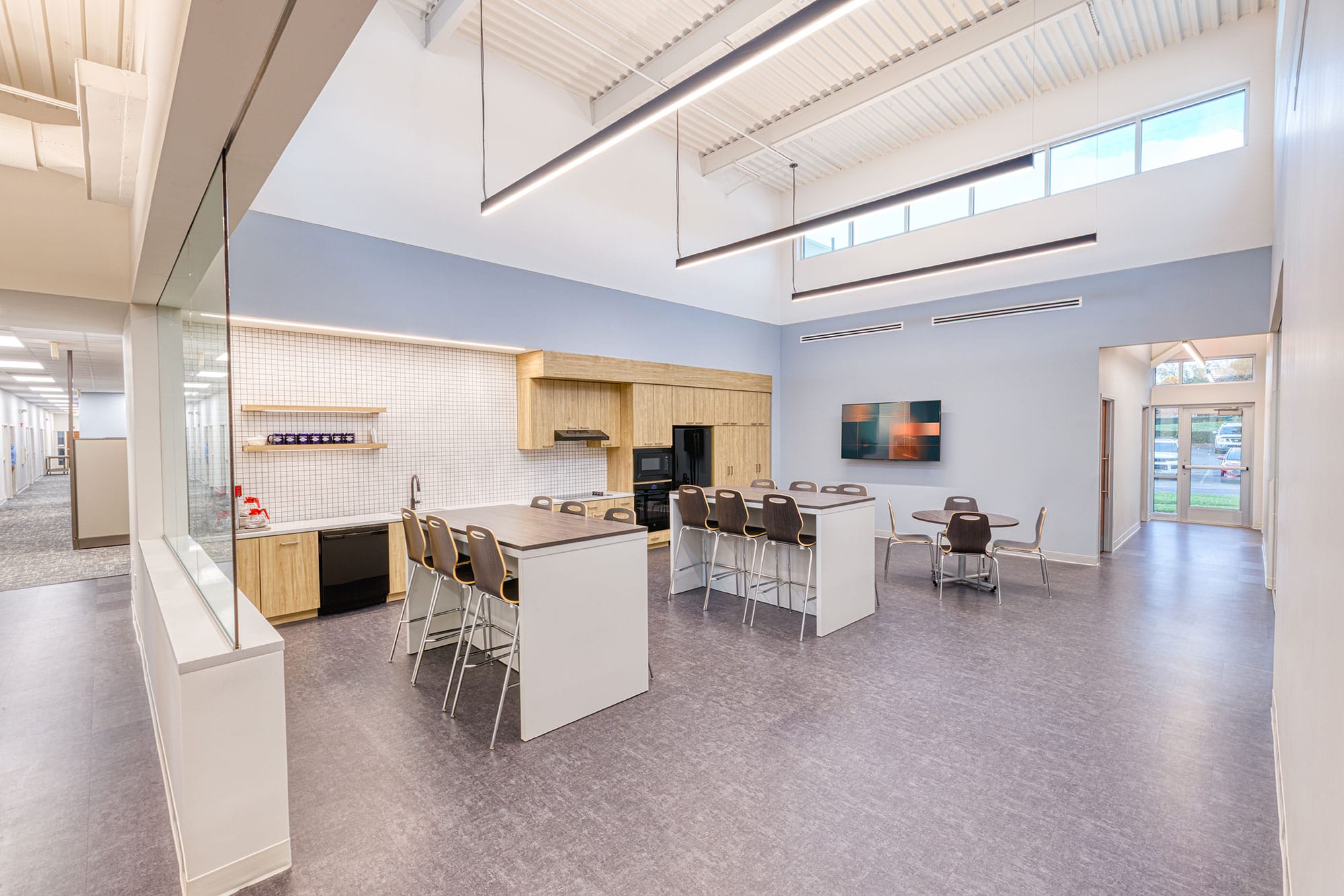 Crowder Construction breakroom in Charlotte, NC with a kitchen island, bar stools and a glass door to the outside, by Ossa Studio