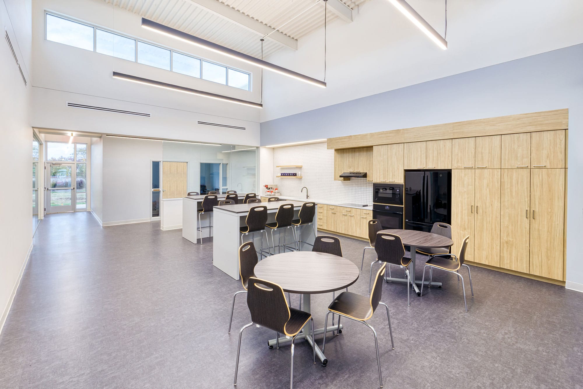 Double-height breakroom at Crowder Construction in Charlotte, NC with wood cabinetry, round tables and clerestory windows by Ossa Studio