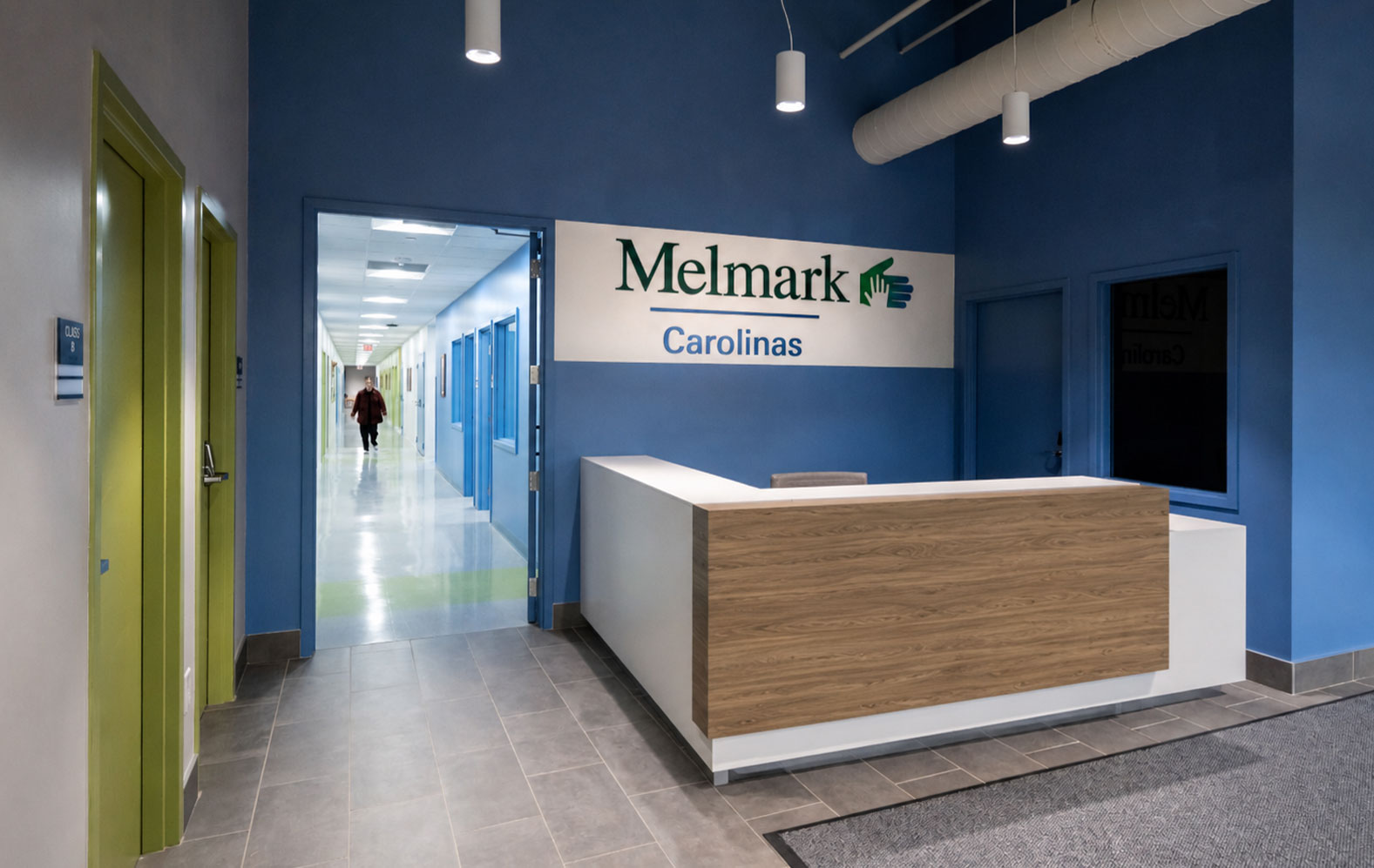 Reception lobby at Melmark Carolinas in Charlotte, NC with a blue wall, wood-front desk and corridor beyond by Ossa Studio