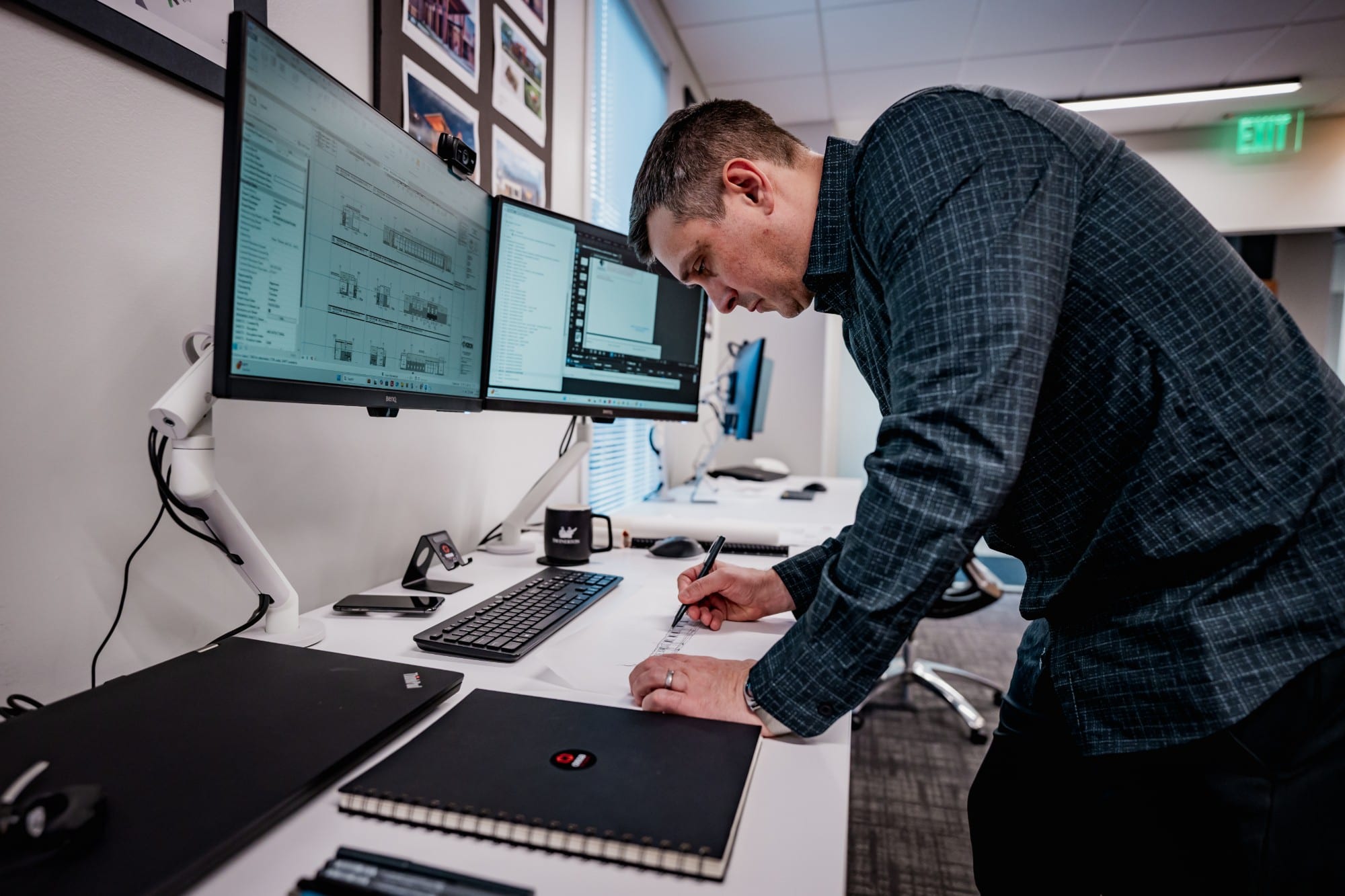 Ossa Studio architect drawing by hand at a standing desk beside two monitors showing building elevations in the Charlotte office