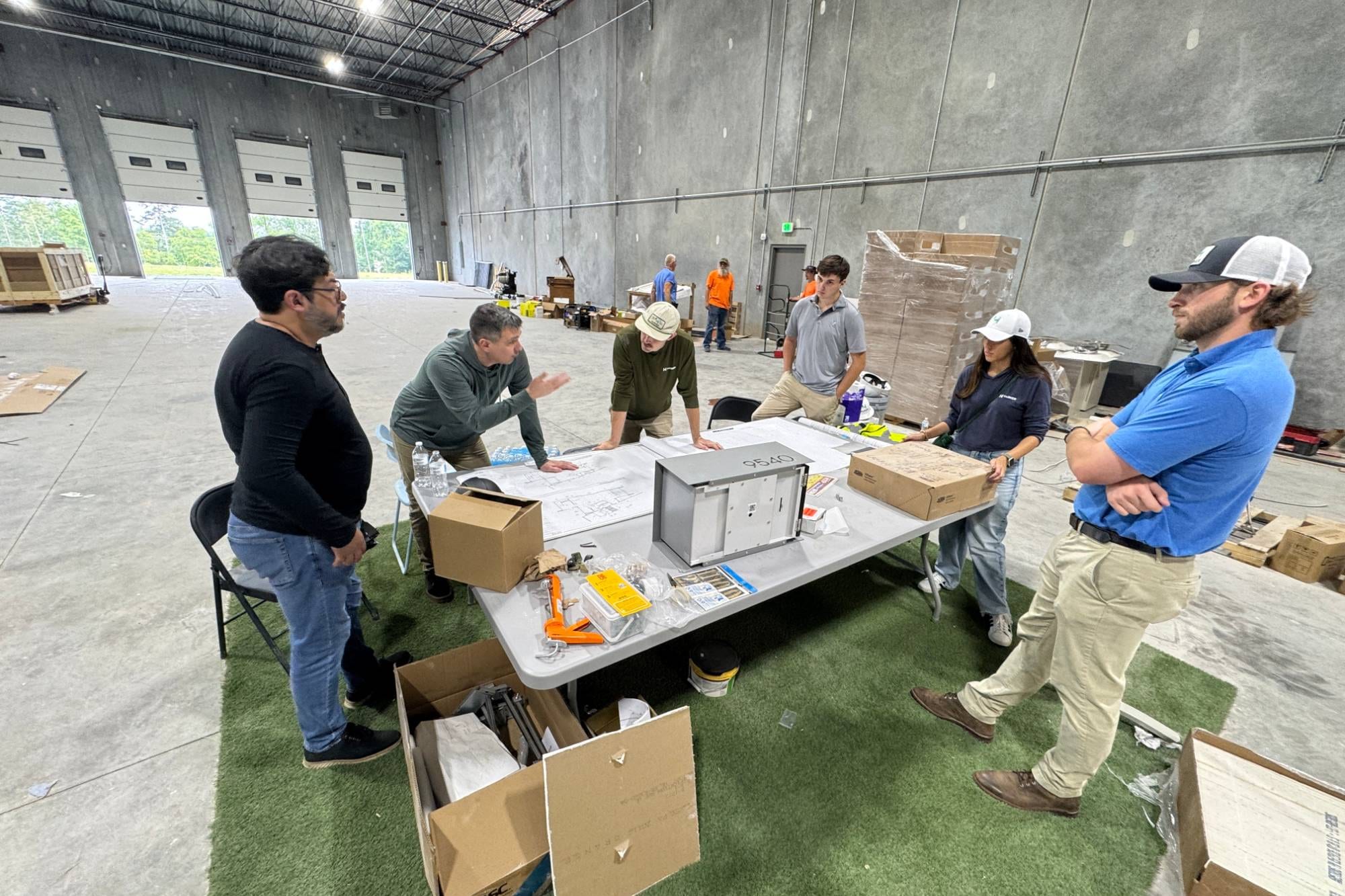 Ossa Studio team and the contractor crew reviewing construction drawings around a table inside an industrial building under construction