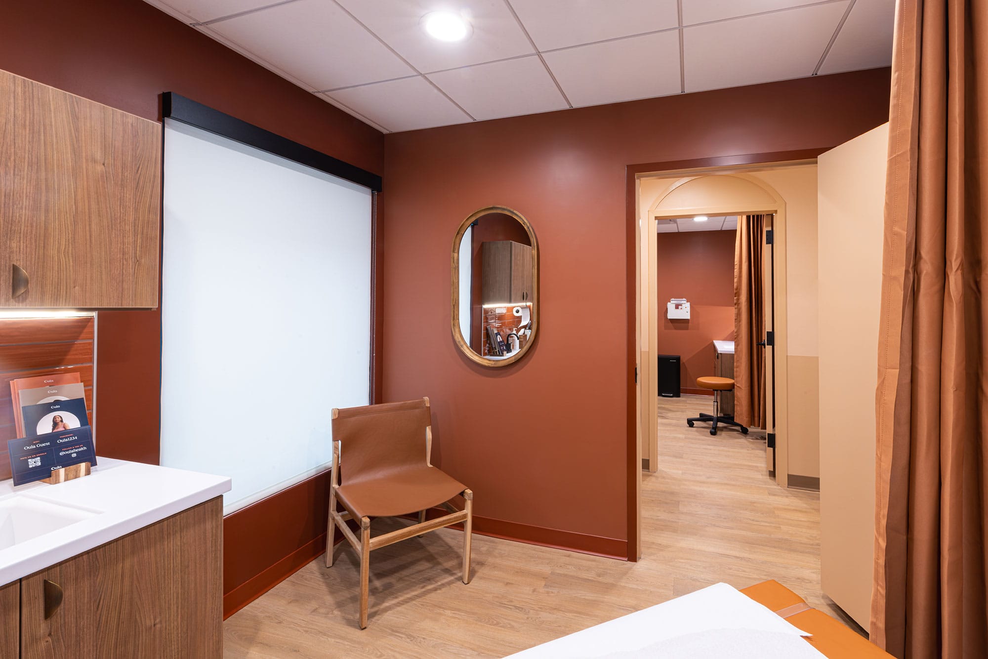 Exam room at Oula Health in Charlotte, NC with warm finishes, wood cabinetry, clinical equipment and custom millwork by Ossa Studio