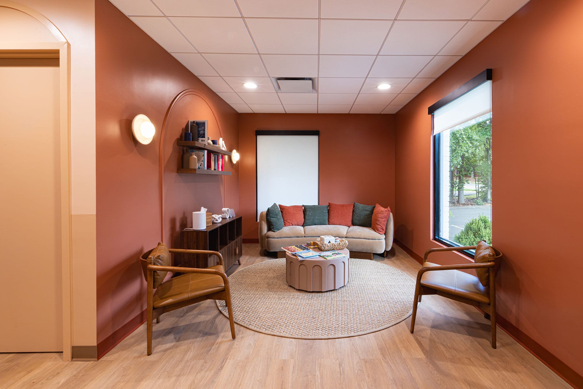 Waiting room at Oula Health in Charlotte, NC with residential-style furnishings, terracotta walls, wood flooring and large windows by Ossa Studio
