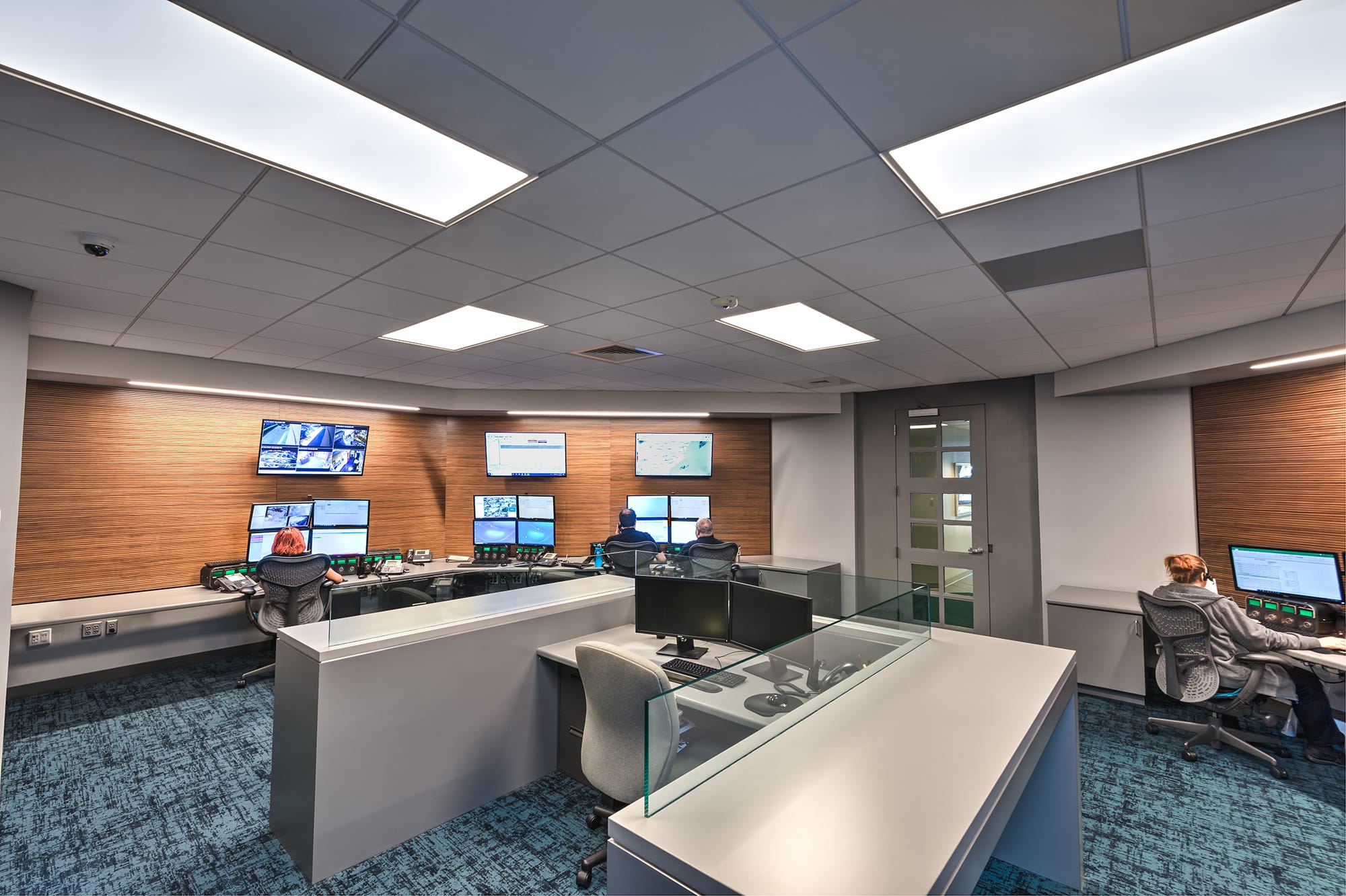 Operator desks along curved wood-paneled walls with wall-mounted screens in the Sonitrol Control Room in Charlotte, NC by Ossa Studio