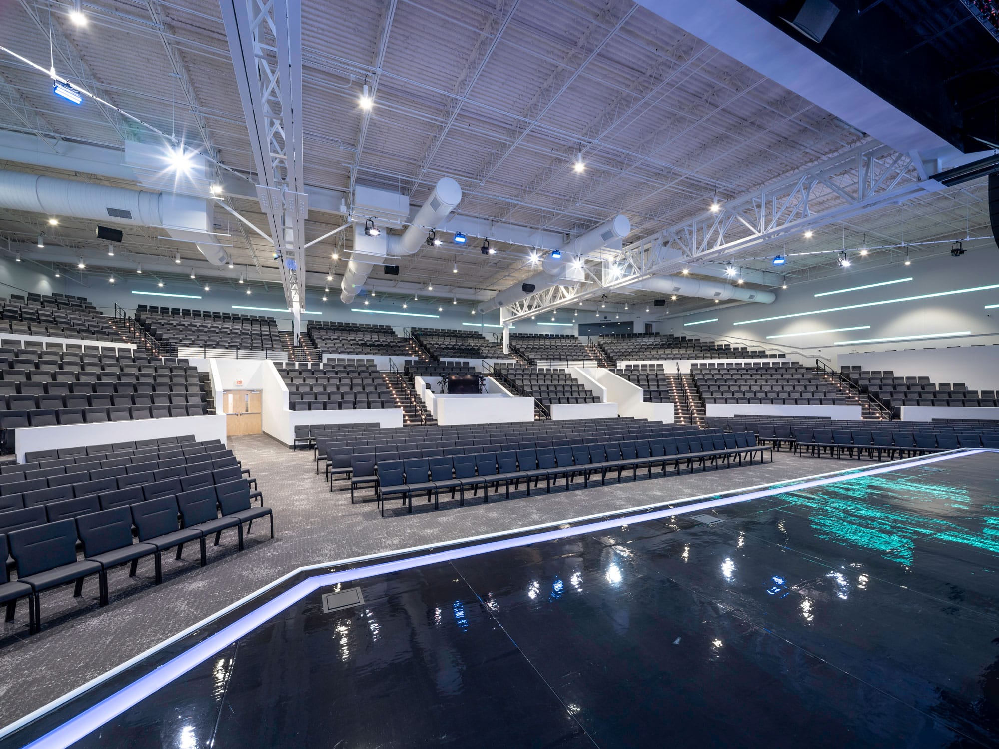 Center aisle through tiered seating to the stage and video screens in the Vizion Church auditorium in Charlotte, NC, by Ossa Studio.
