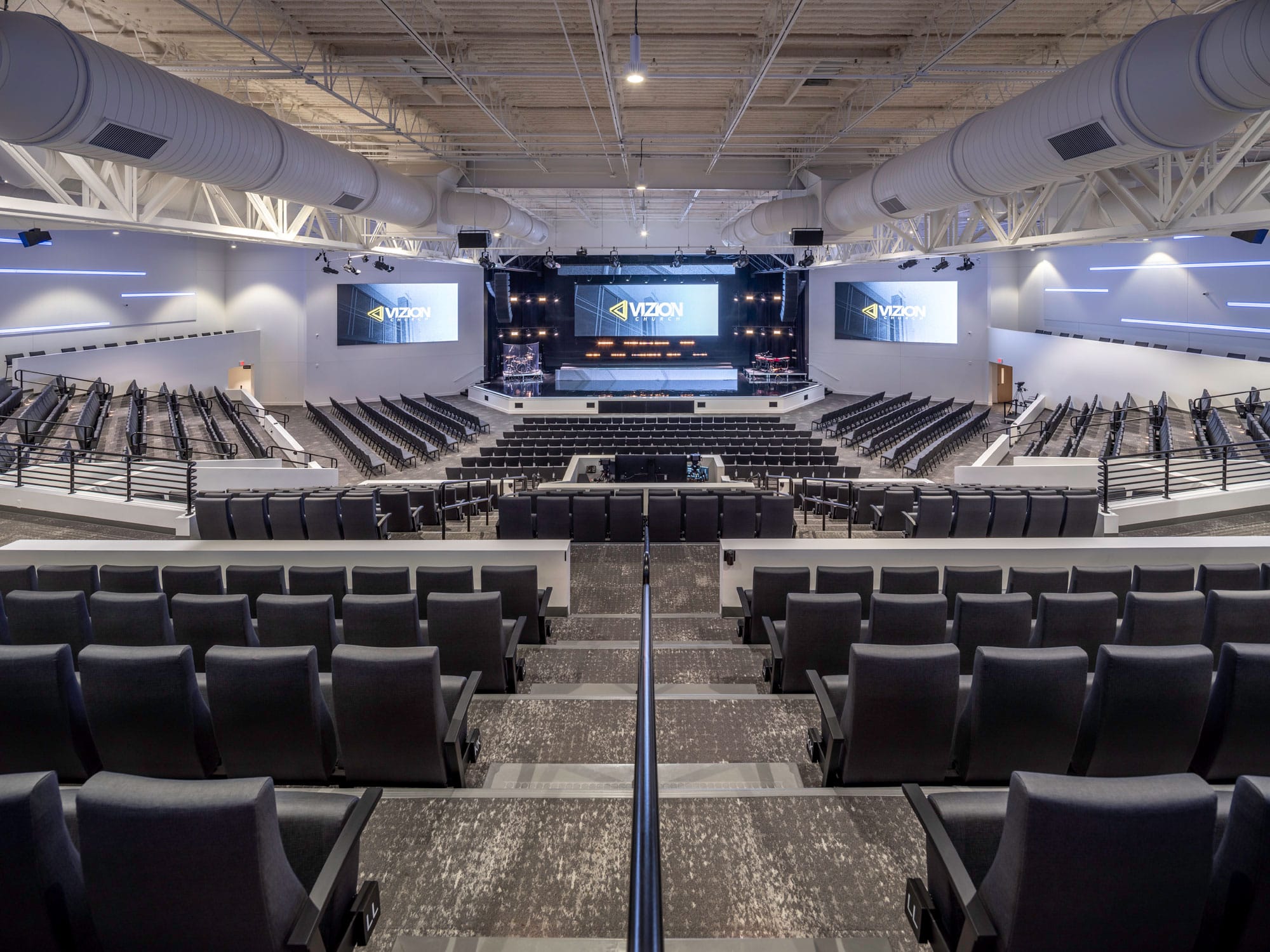 Vizion Church auditorium in Charlotte, NC seen from the upper seating with tiered seating, central stage and video screens