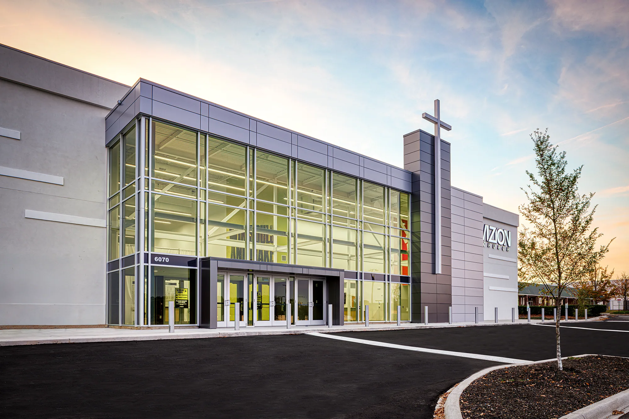 Two-story glass entrance glowing at dusk beside the cross tower of Vizion Church in Charlotte, NC, a church converted by Ossa Studio.